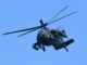 Američki jurišni helikopter AH‑64 Apache u letu, snimljen iz blizine u niskom preletu iznad terena, s jasno vidljivim rotorskim krilima i naoružanjem.